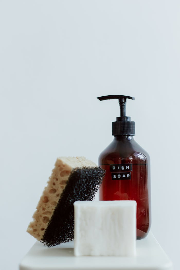 Aesthetic shot of dish soap, sponge, and soap bar on white backdrop.